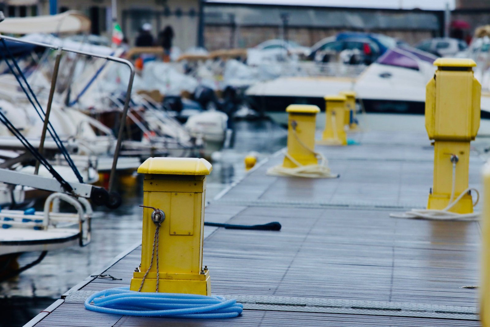 A row of yellow quayside service pedestals along a wet marina pontoon, with a blue hose coiled on the deck and moored boats behind.